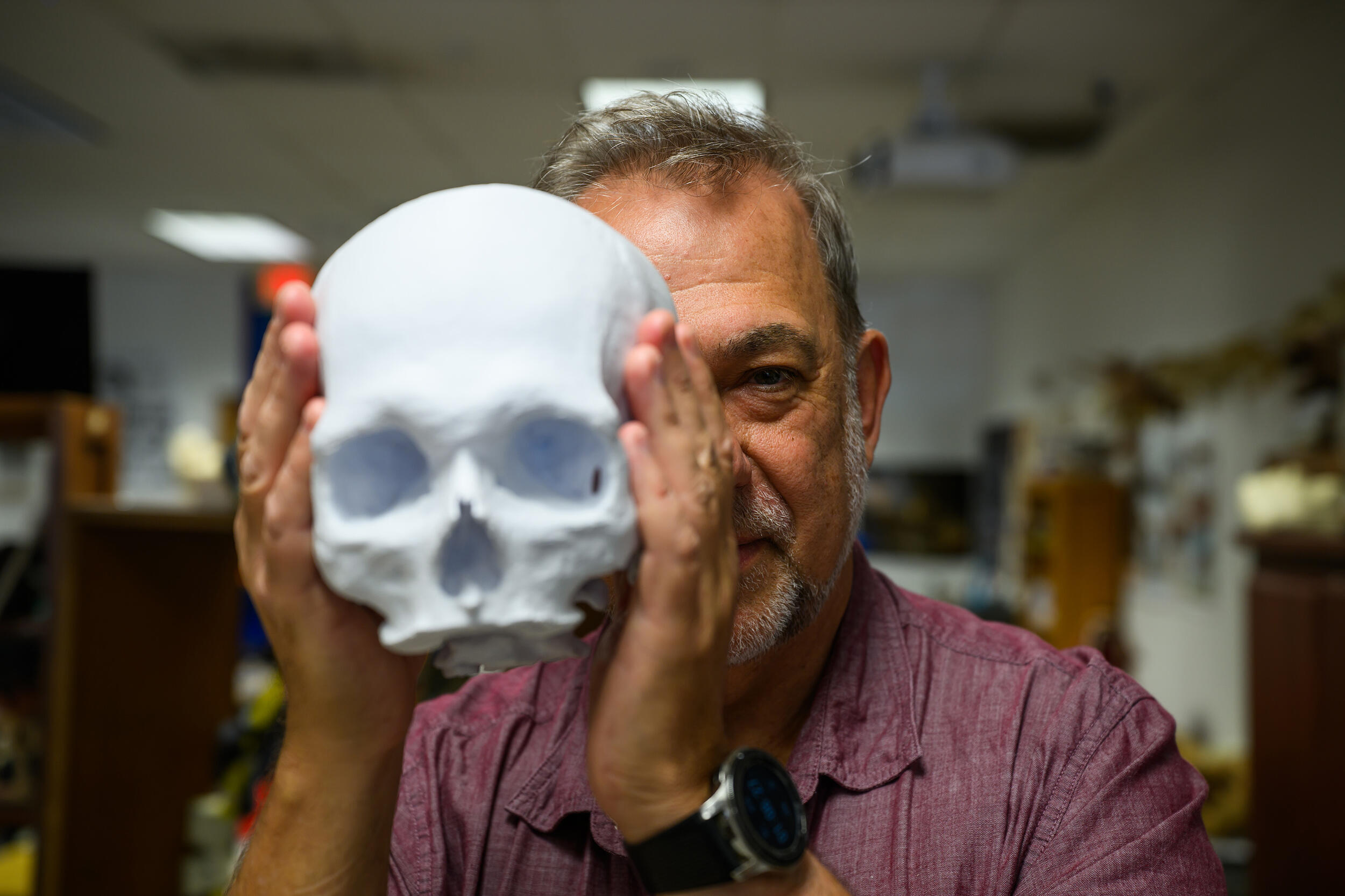 A photo of a man holding a fake skull in front of the left side of his face,. 