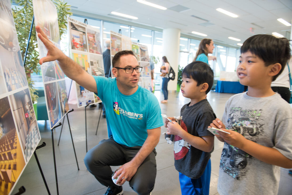 Adult man shows images of a new children's hospital to two children.
