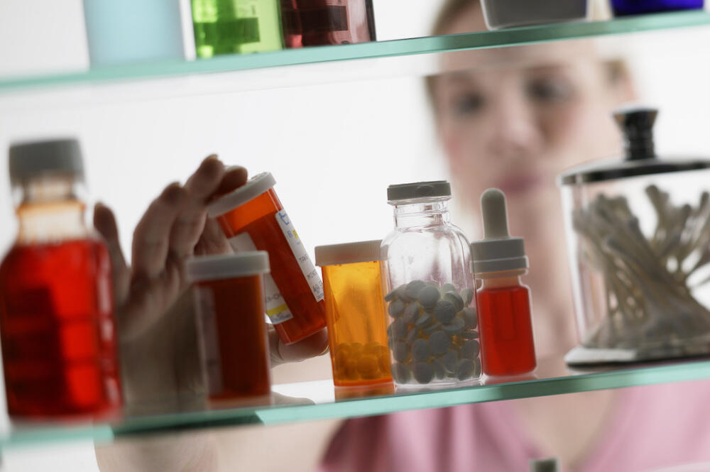 Woman looks at prescription medication in bathroom cabinet. 