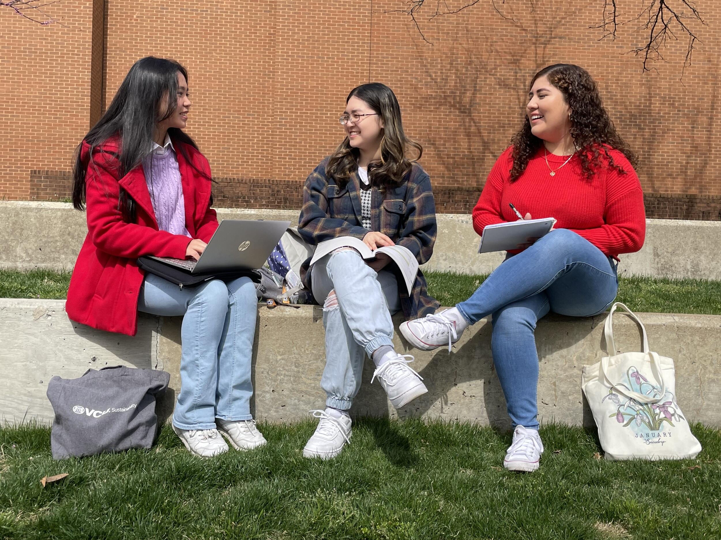 A photo of three women sitting outside and talking to each other. 