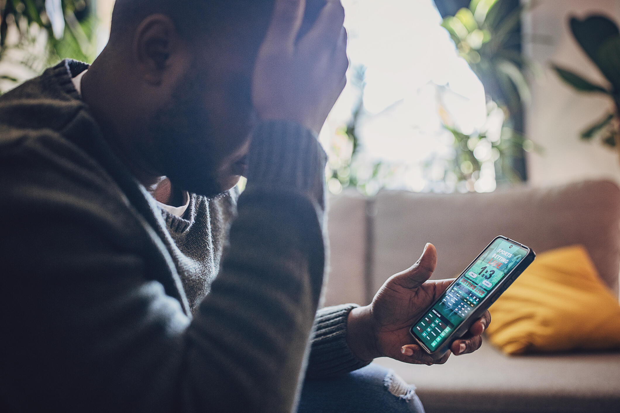 A photo of a man holding his head in his hand while looking at a sports betting app on his phone.