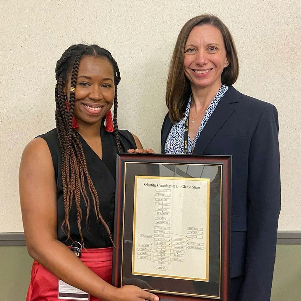 Two women standing next to each other, one is holding a framed document 