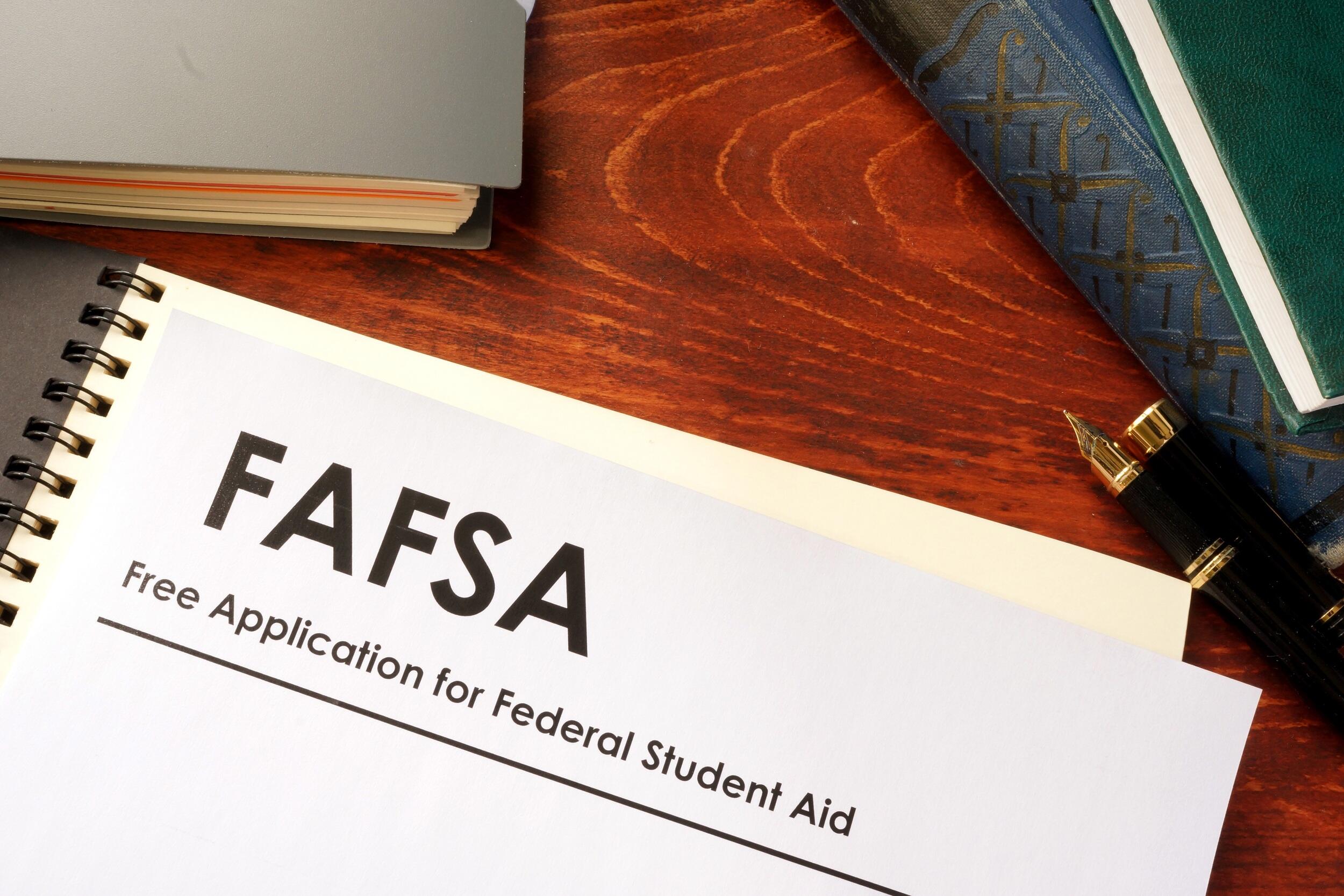 A piture of a white piece of paper that says \"FAFSA Free Application for Federal Student Aid\" on top of a notebook on a desk