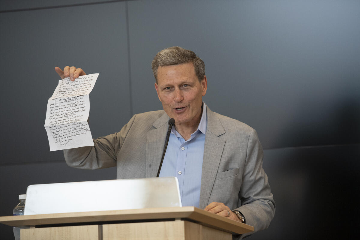 A man standing at a podium holding a piece of paper up with his left hand. 