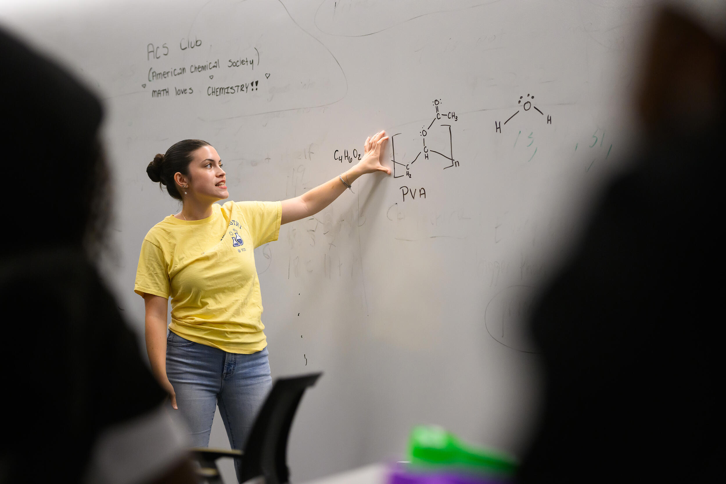 A photo of a woman pointing to a white board. 