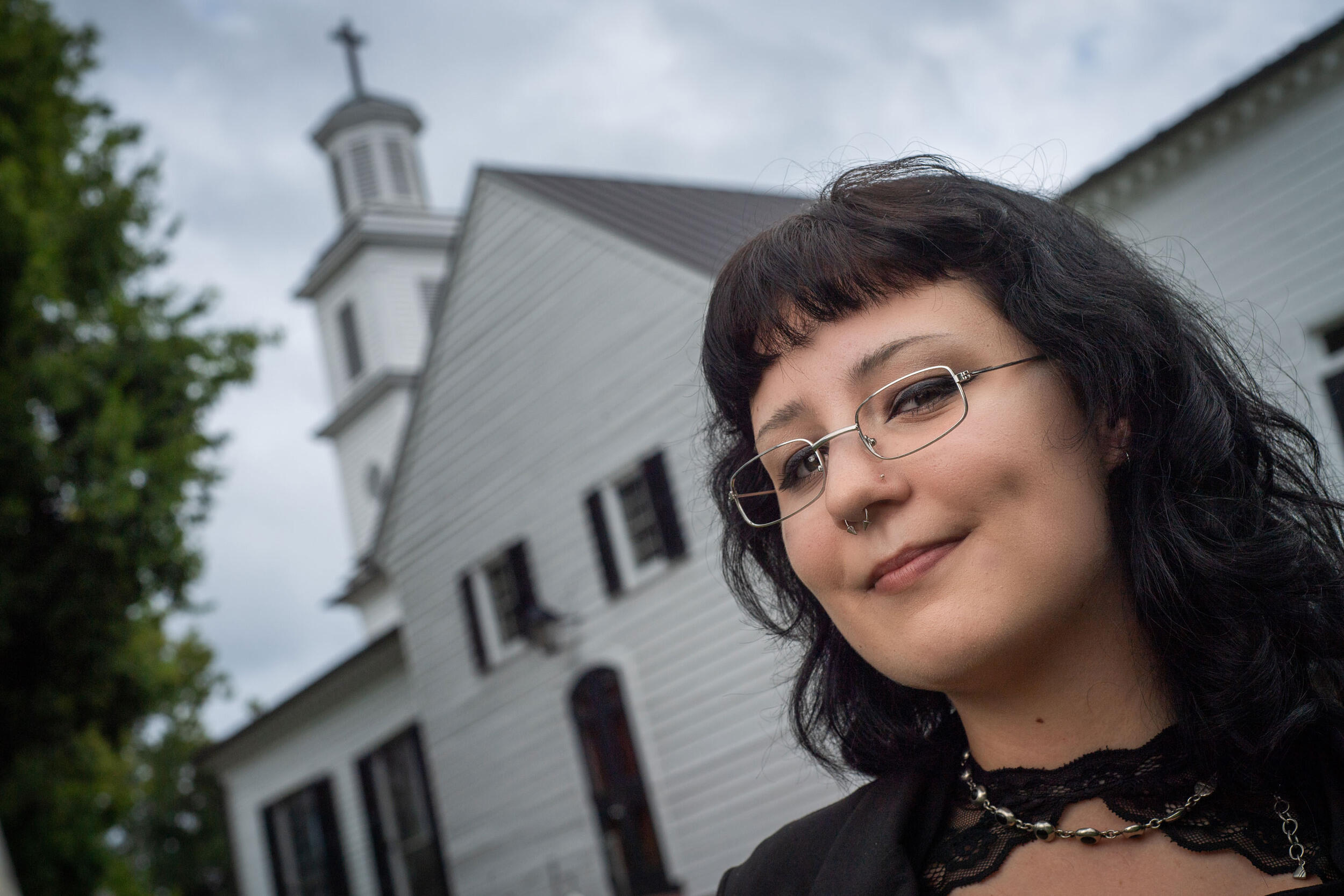 A woman in glasses smiles with a church in the background.