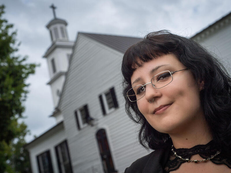 A woman in glasses smiles with a church in the background.