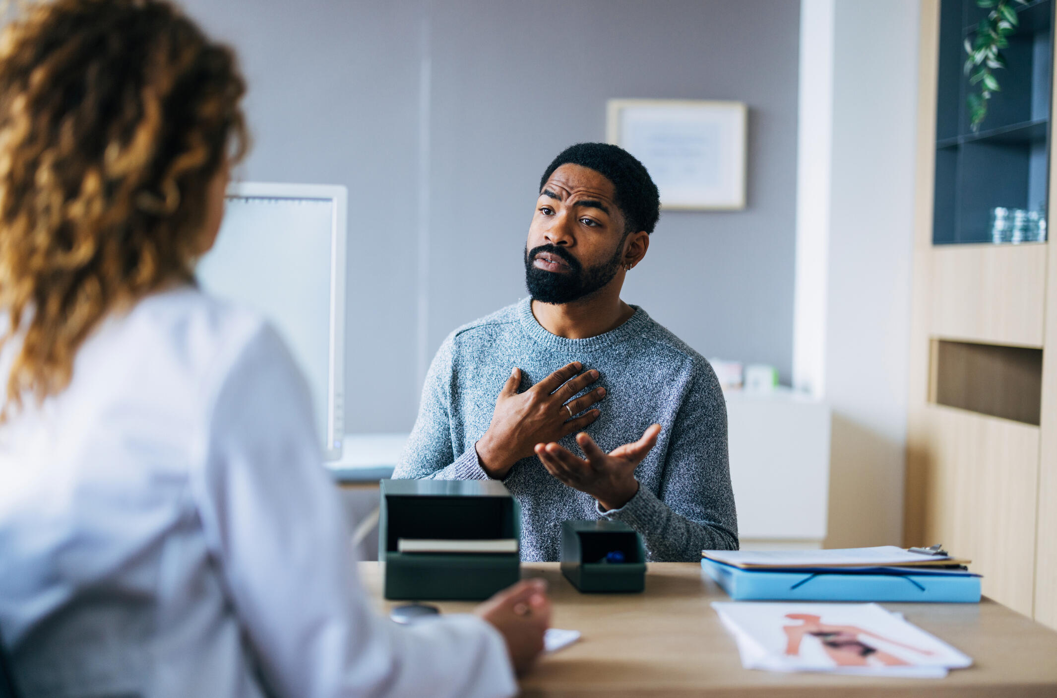 A man gestures while speaking with a woman in a white lab coat, illustrating the concept of a sickle cell disease patient describing their pain.