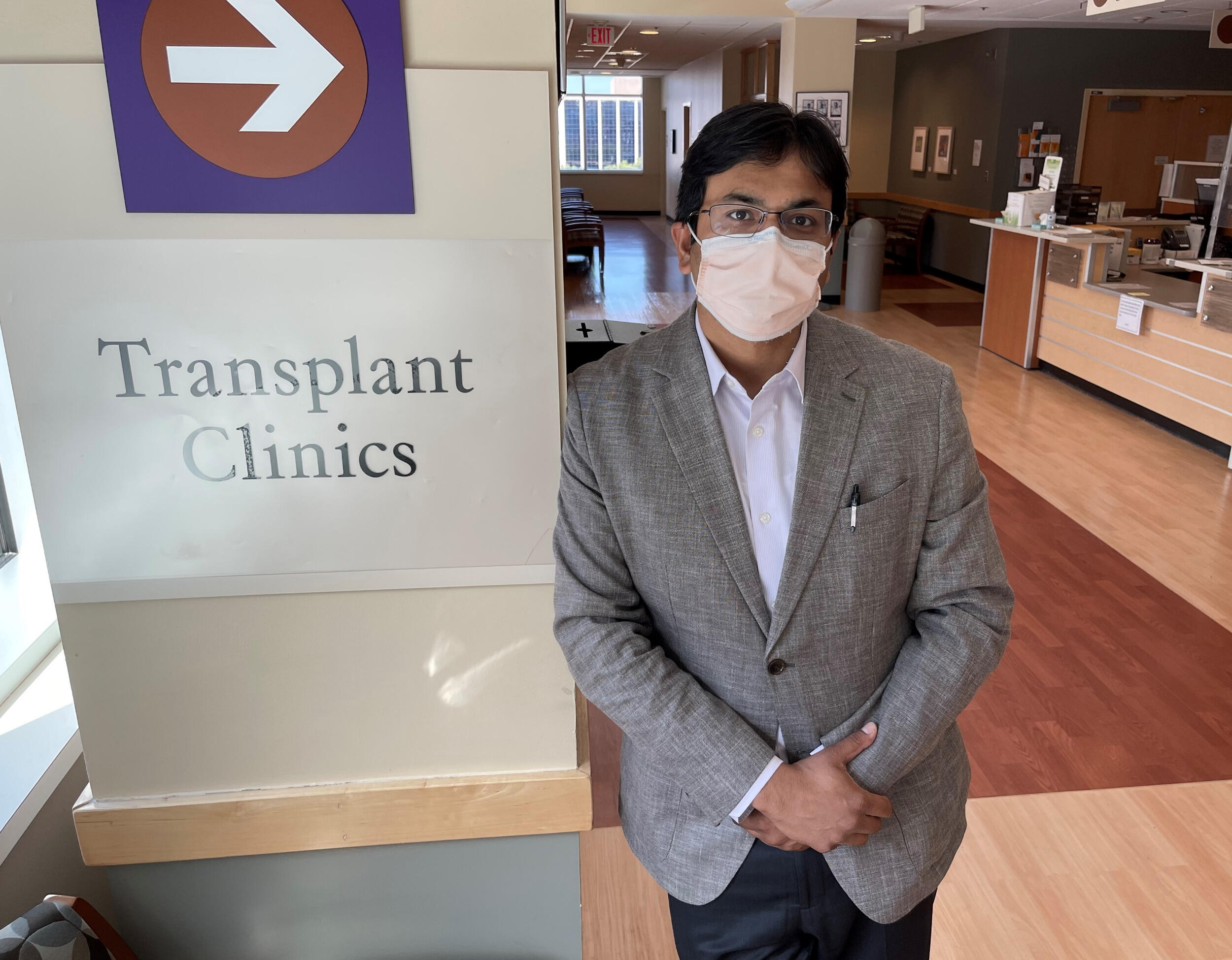 Portrait of man in mask and jacket next to Transplant Clinics sign.