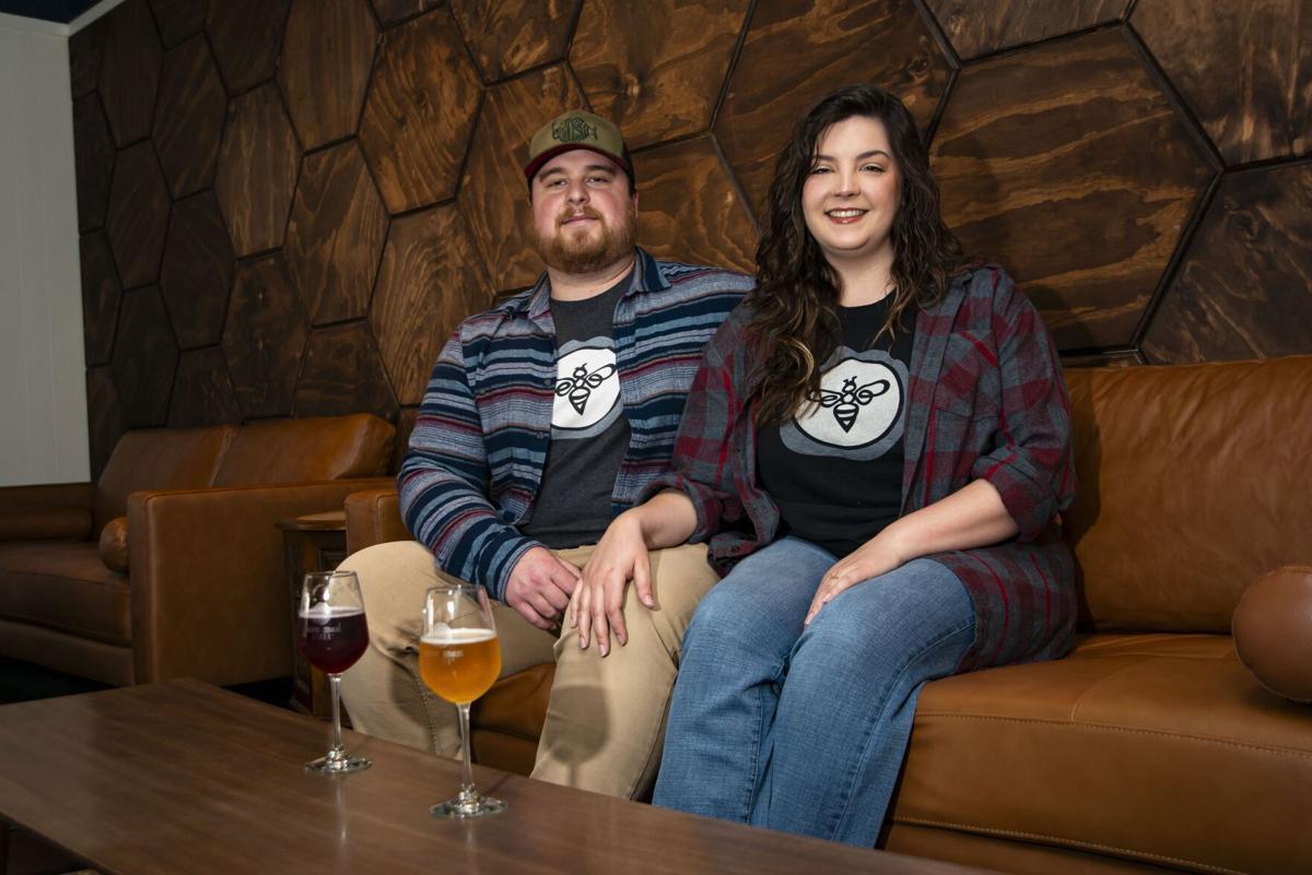 A photo of a man and a woman sitting on a brown leather couch. In front of the couple is a wooden coffee table with two tall stemmed glasses of cider on it. 