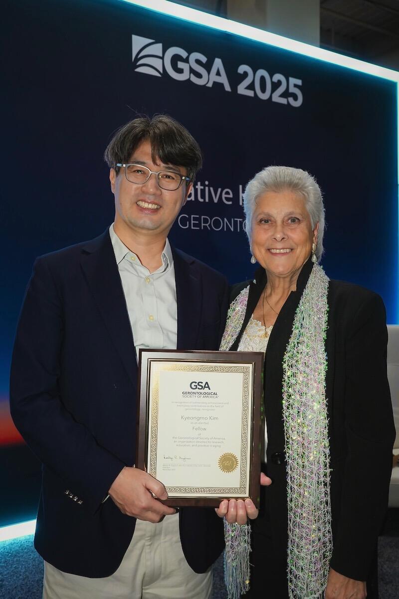 A photo of a man holding a plaque standing to the left of a woman. Both people are smiling. 