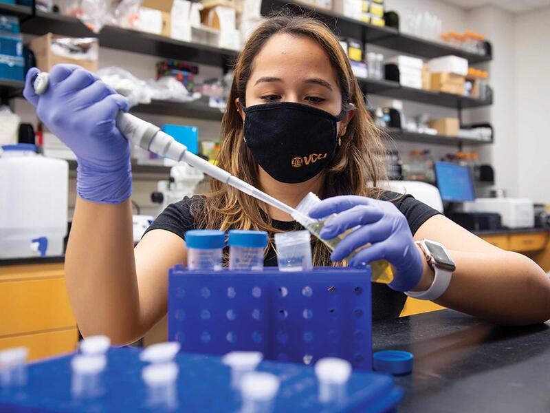 A woman wearing a face mask and rubber gloves holding a beaker