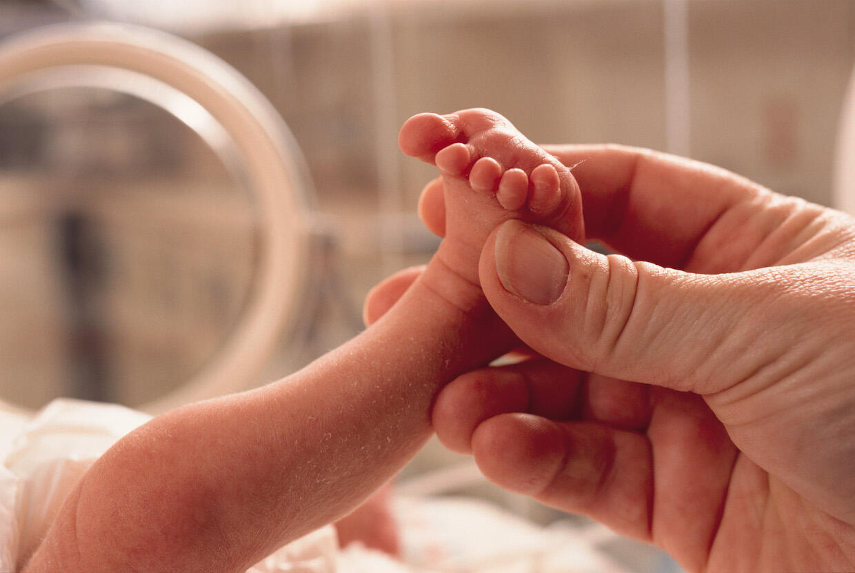 A person cradling an infant's foot with their fingers.