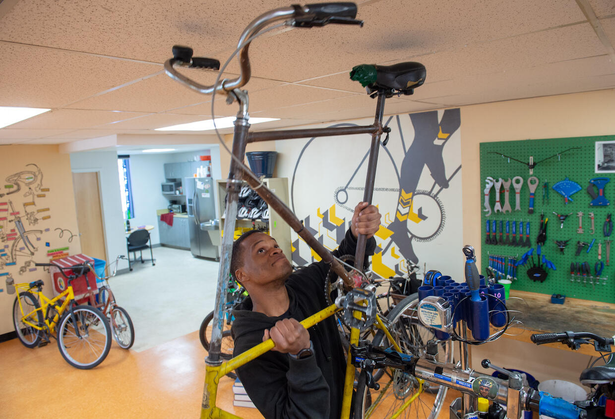 Man lifting tall bike inside bike shop; handlebars are almost touching ceiling.