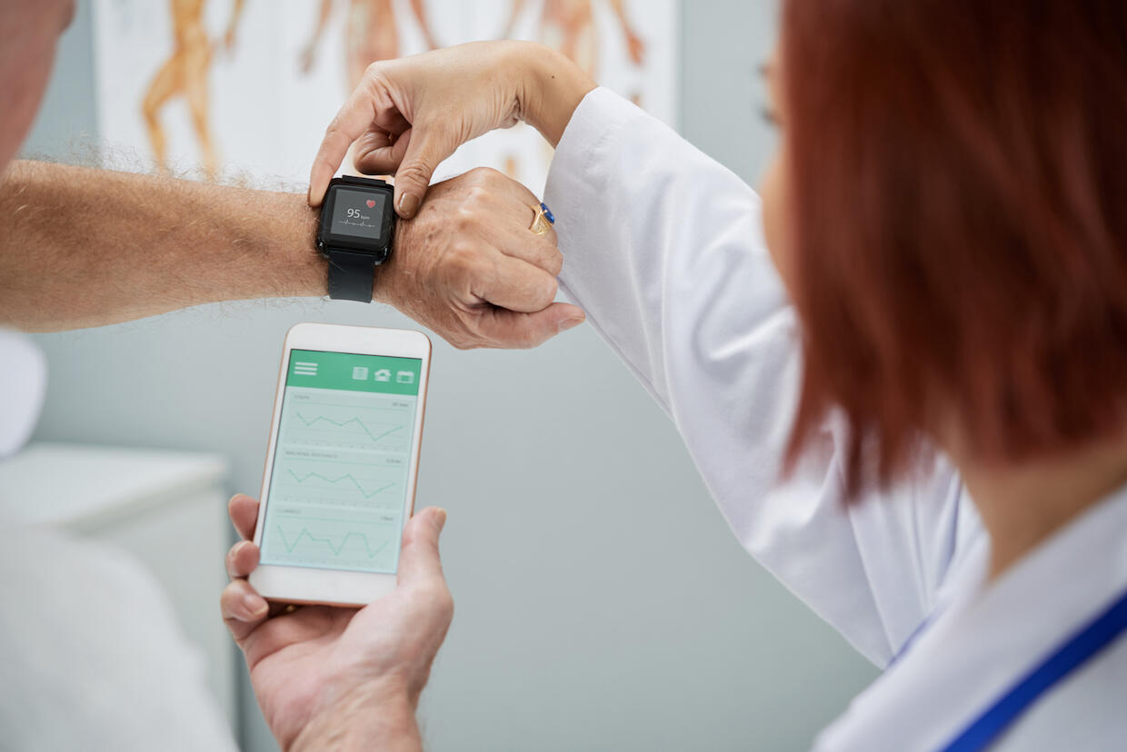 A doctor reviews information on a patient's smartwatch and phone.