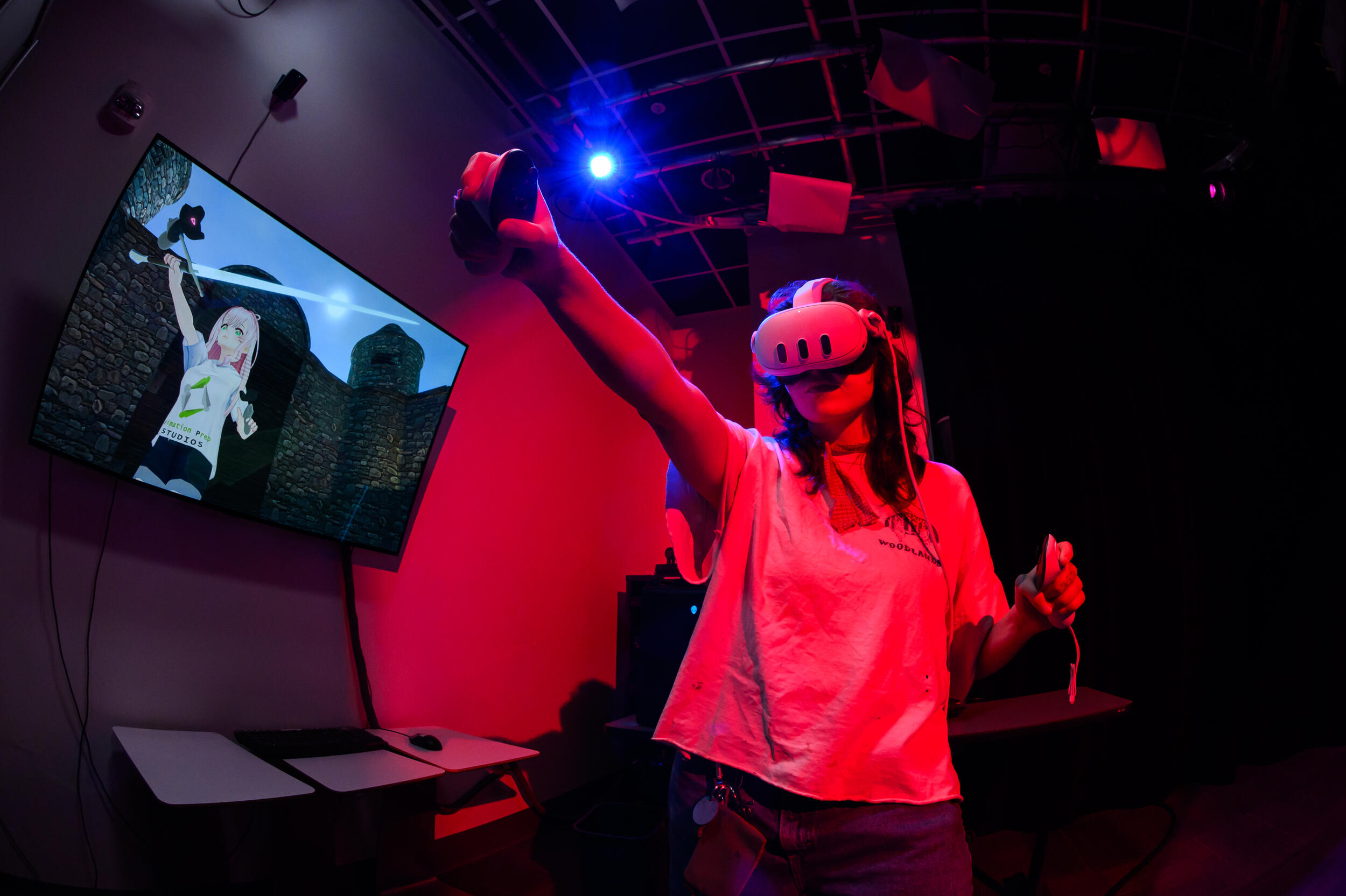 A photo of a woman wearing a 3D headset and holding two remotes in her hands. Behind the woman is a screen that shows a 3D anime girl making the same motion as the woman. 