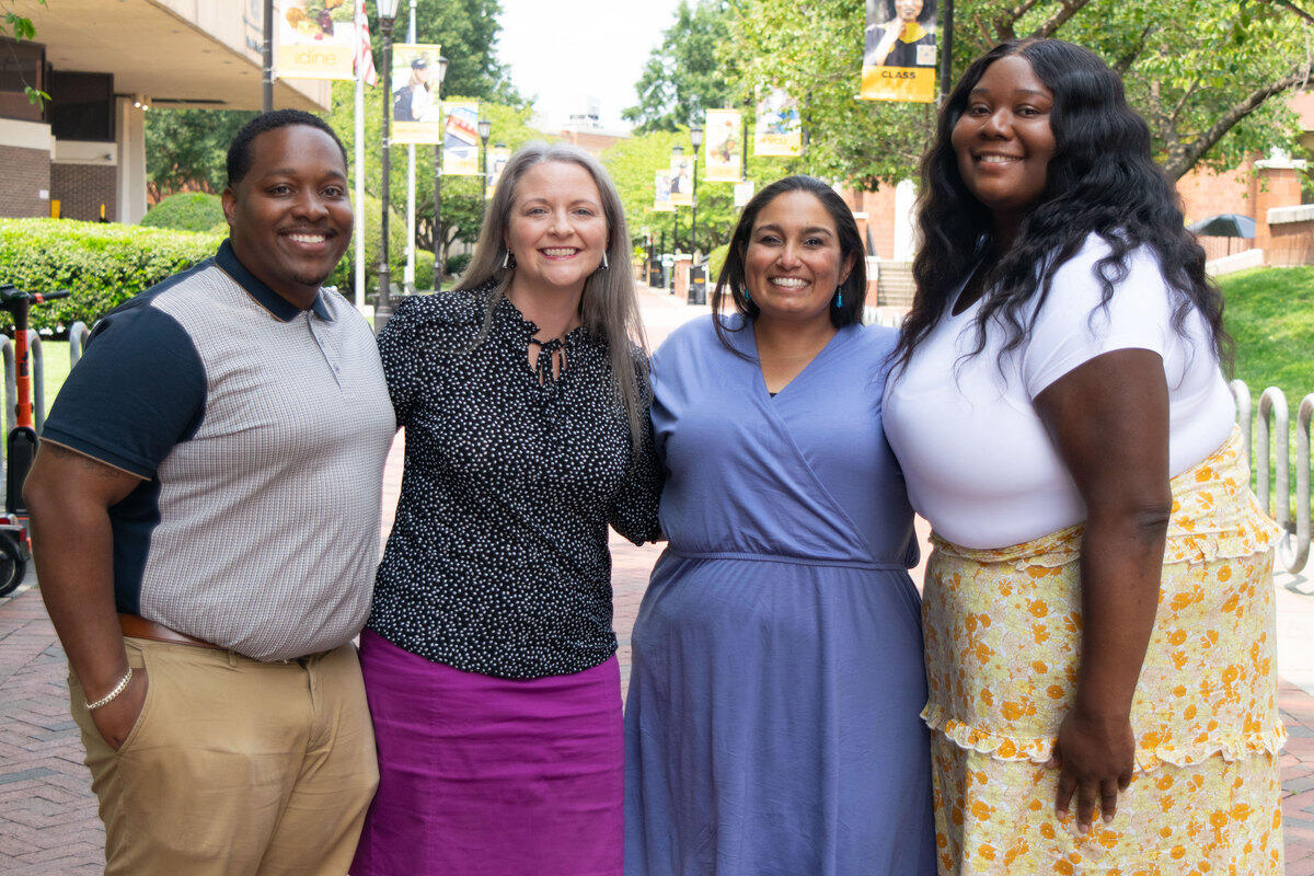 A photo of four people standing outside in the VCU Student Commons plaza and smiling. 