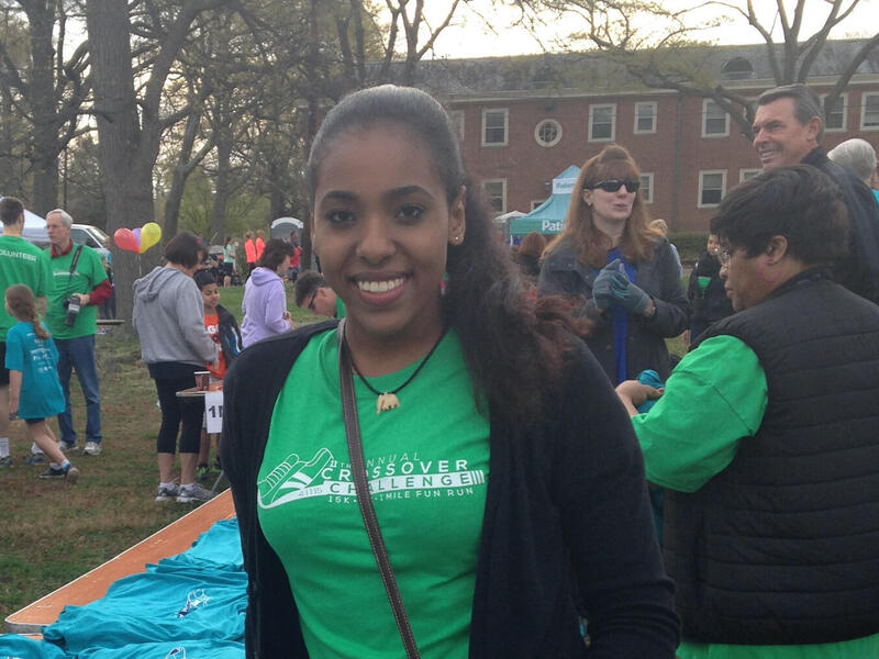A woman in a green shirt smiles and leans on a table filled with T-shirts.