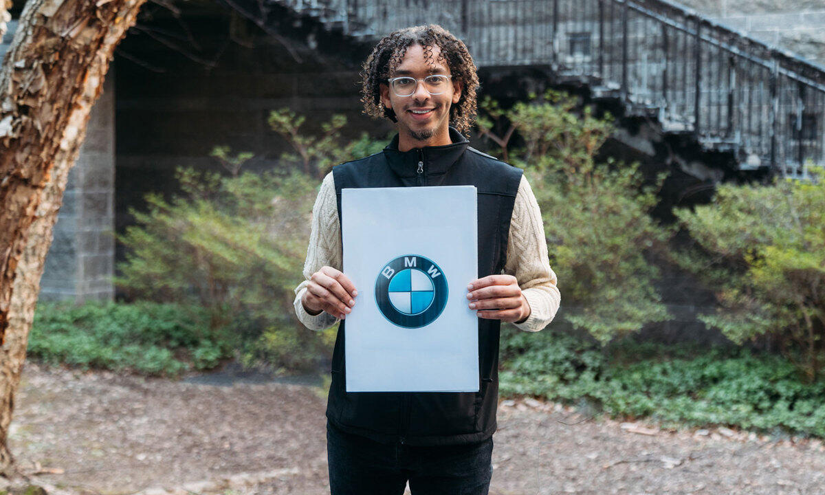 A photo of a man standing outside holding a piece of paper with the BMW logo on it. 