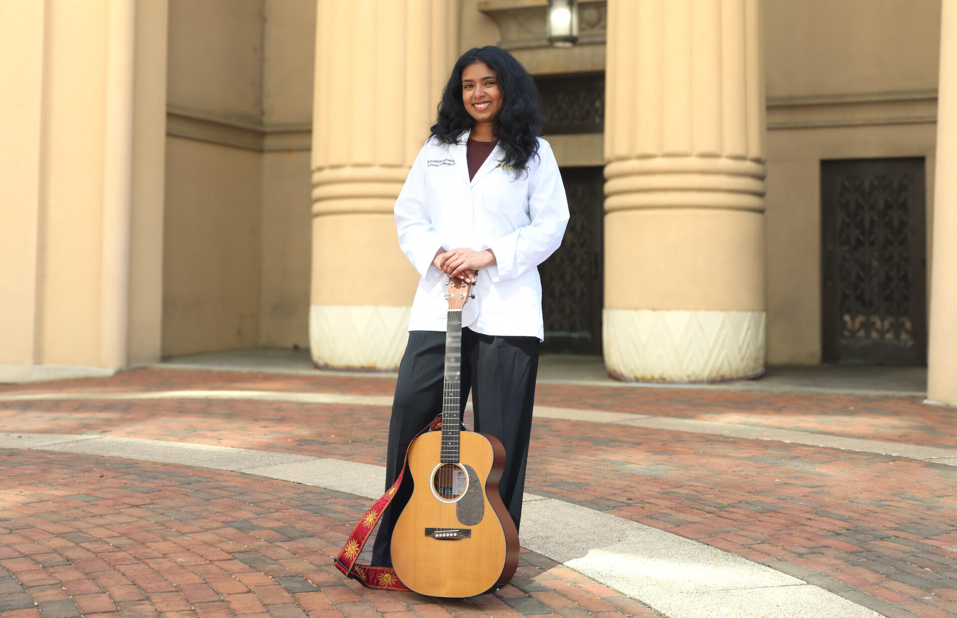 A woman in a white coat stands and holds a guitar.