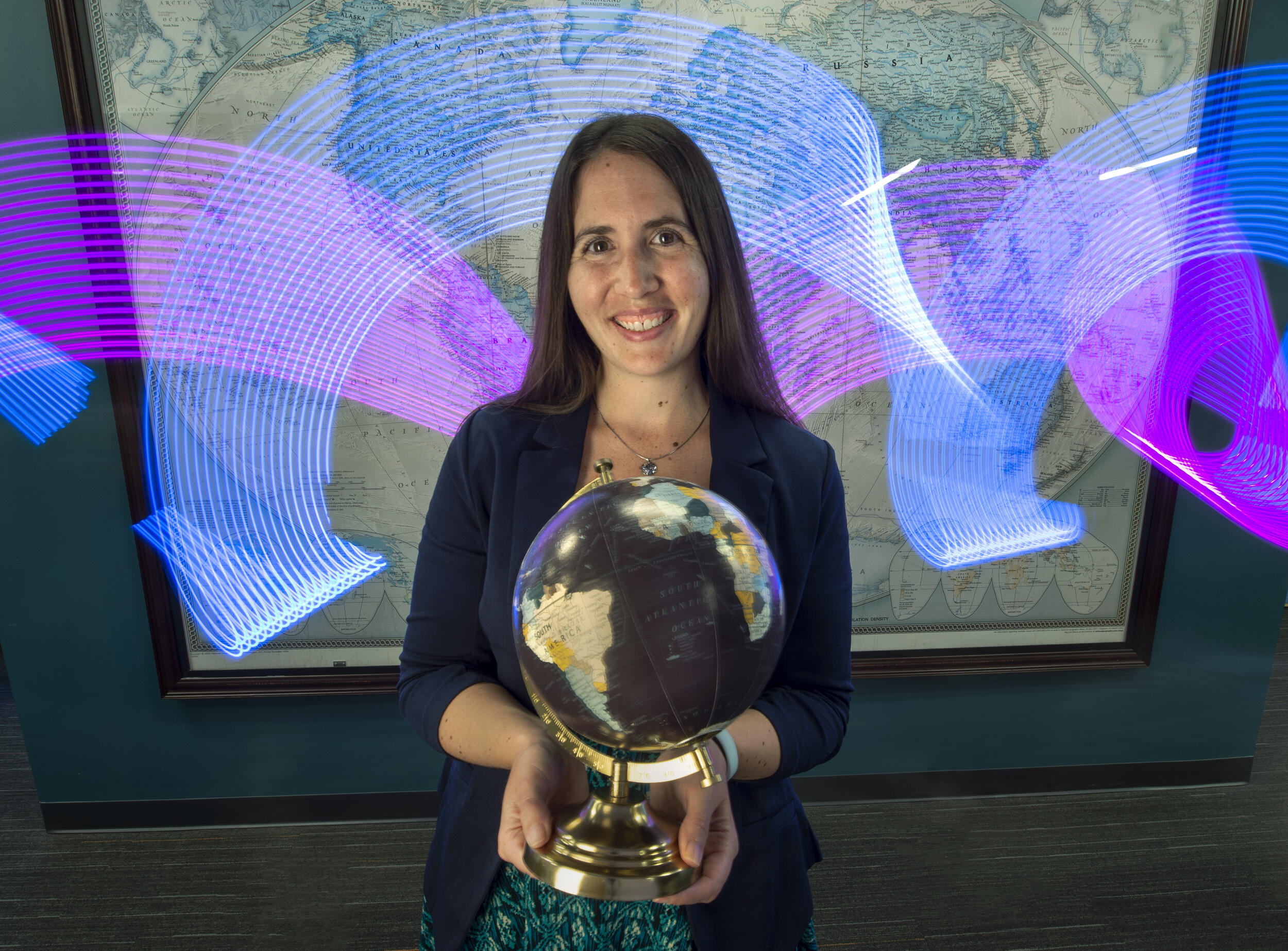 A photo of a woman holding a globe in front of a map