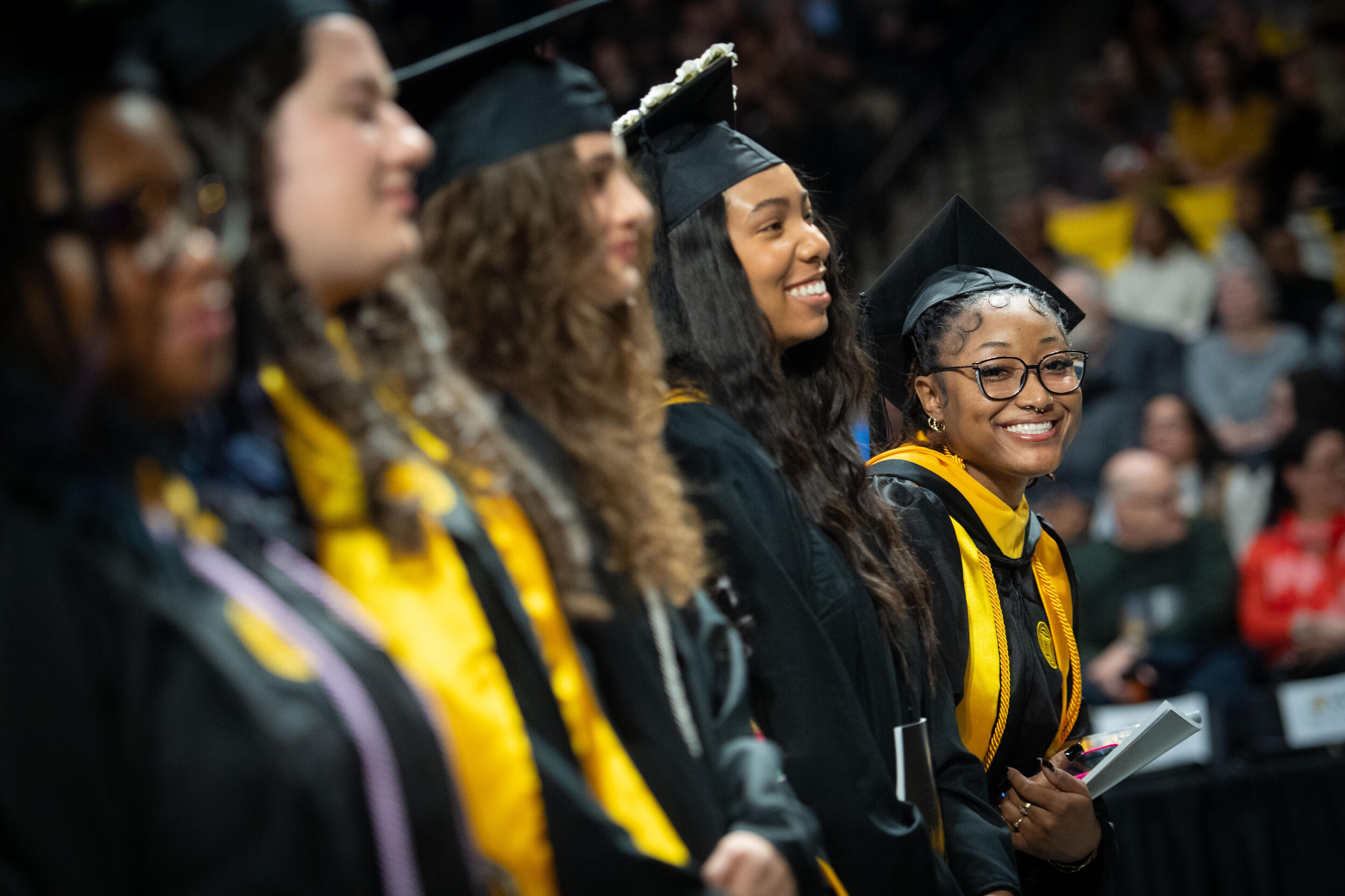 A row of five smiling women wearing caps and gowns.