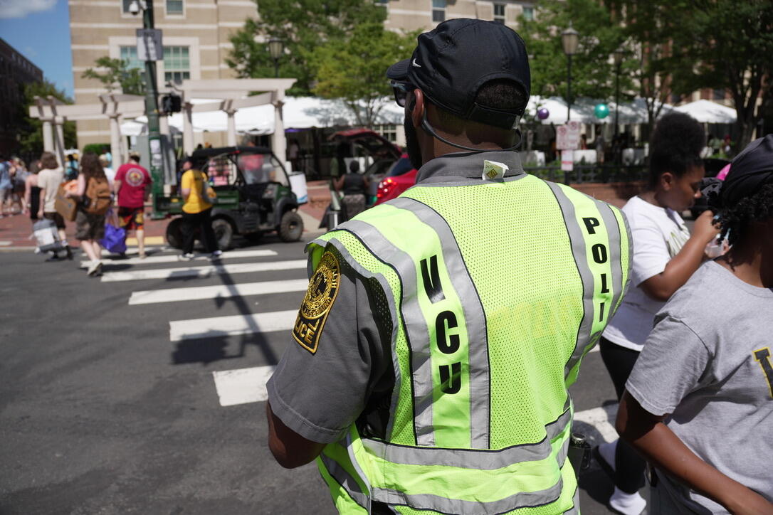 A photo of a police officer wearing a visability vest standing at a cross walk where people have just walked to the other side of the street. 